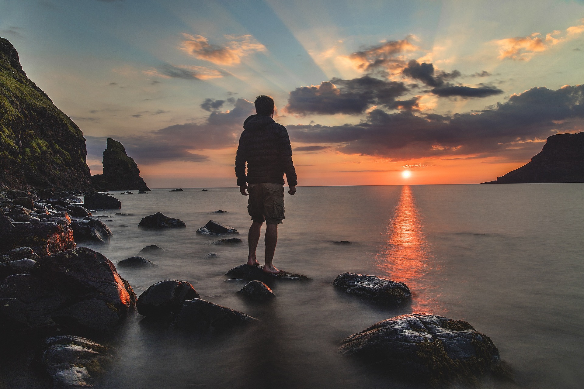 man bij rotsen met oceaan en zonsondergang
